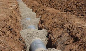 Underground drainage pipes in a gravel-lined trench, with a topographic survey helping guide the planned sewer route